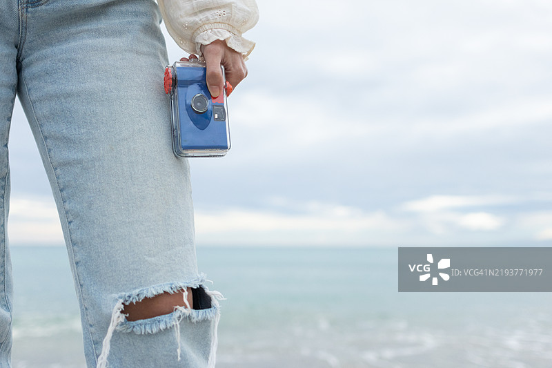 一位女性在海边度假时使用一次性傻瓜相机。图片素材