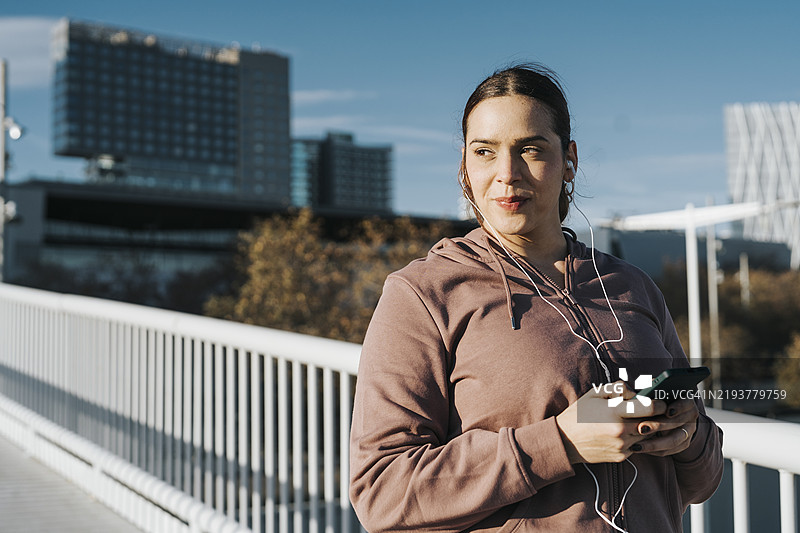 身材健美的女性佩戴无线耳机，在户外健身时查看智能手机，暂停进行锻炼间歇。图片素材