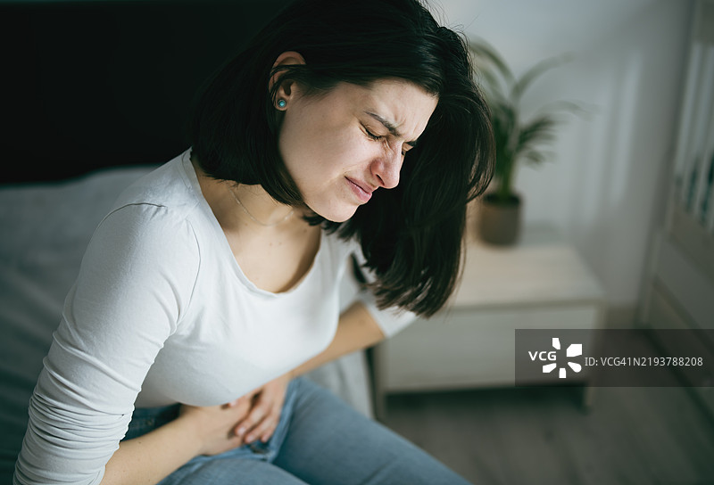 年轻女人感到腹部不适，双手抱住肚子。图片素材