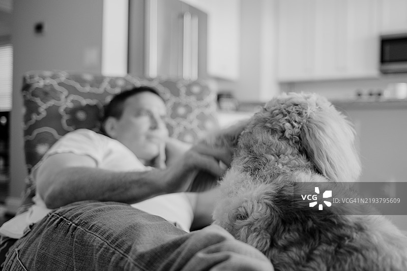 男人在椅子上放松时抚摸他的狗图片素材