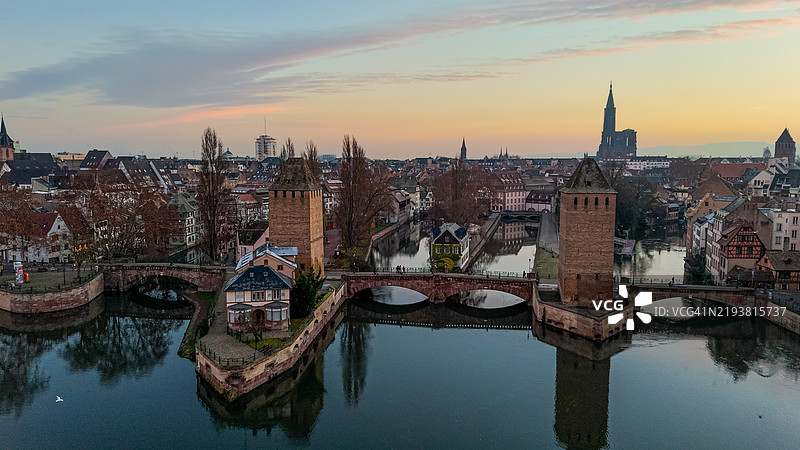 日出时分的斯特拉斯堡城市全景，展示了历史建筑和小法国区，突显了覆盖桥塔和沃邦水坝，展现了中世纪桥梁和标志性的斯特拉斯堡大教堂。图片素材