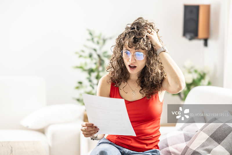 震惊的年轻女性在阅读她收到的律师信件、办公室或水电费账单。图片素材