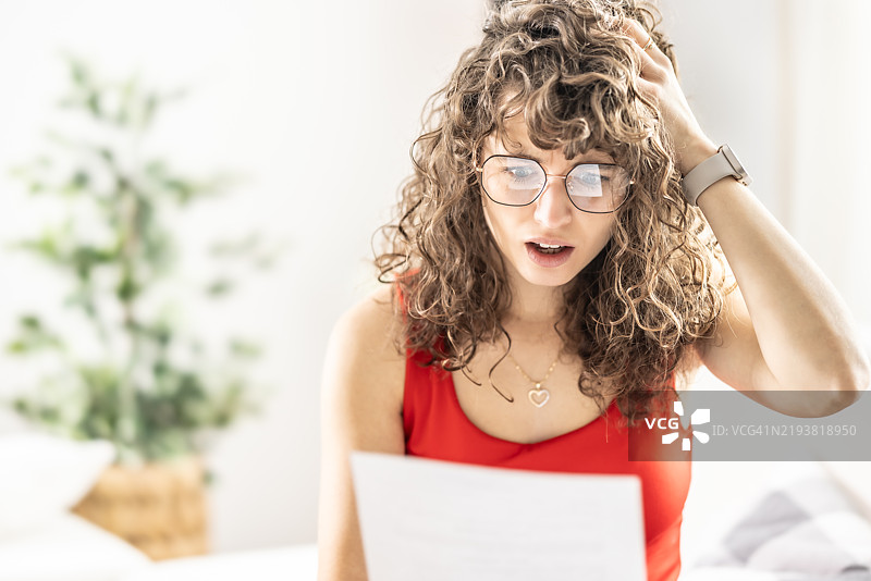 震惊的年轻女性在阅读她收到的律师信件、办公室或水电费账单。图片素材