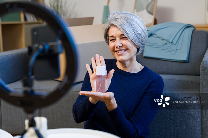 微笑的成熟网红在家中录制视频，展示美容产品图片素材