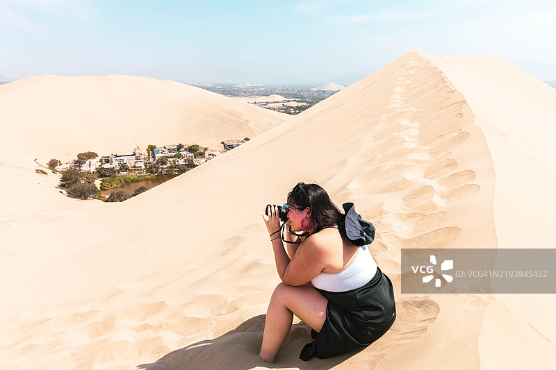 在秘鲁的华卡奇纳绿洲，女性在最高的沙丘上拍照图片素材
