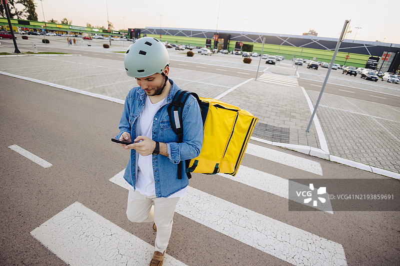背着黄色背包的快递员一边走一边使用手机图片素材
