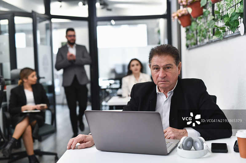 坐在办公室里的权威男性，面前放着笔记本电脑，严肃地看着镜头。图片素材