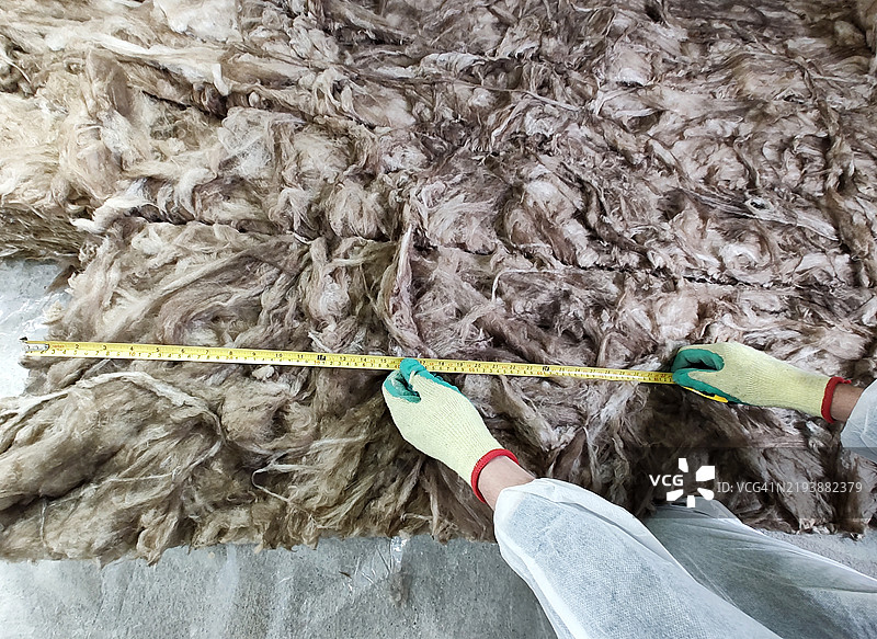 工人正在测量玻璃棉，以便为后续的石膏板包覆进行隔热和隔音处理。图片素材