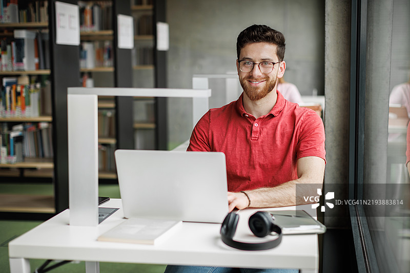 年轻学生在图书馆使用笔记本电脑时微笑的肖像图片素材