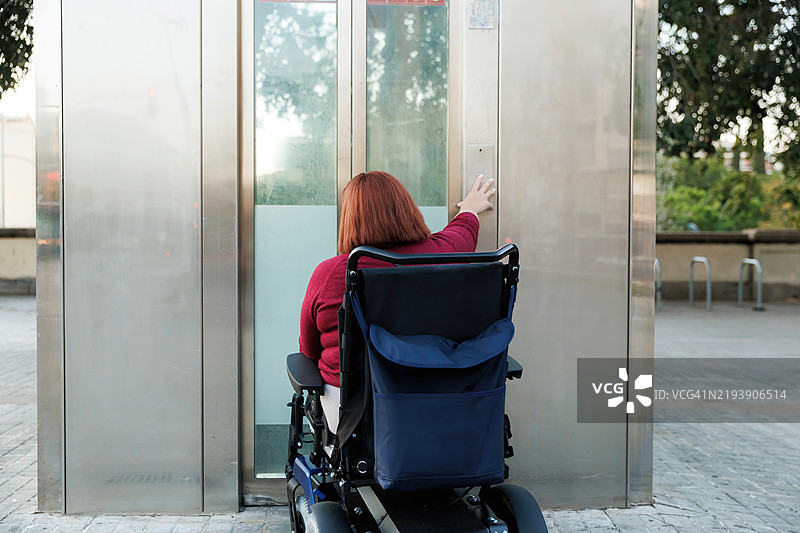 一位白人女性残疾人士正在按电梯按钮，适合残疾人士使用的无障碍环境，配备现代轮椅。图片素材