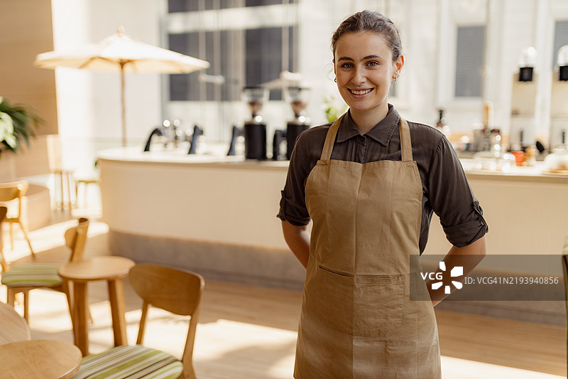 友好的女性咖啡师站在阳光明媚的咖啡馆柜台后面图片素材