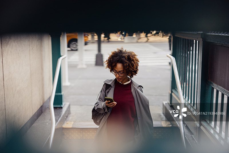 年轻女性在城市环境中使用智能手机走出地铁站图片素材