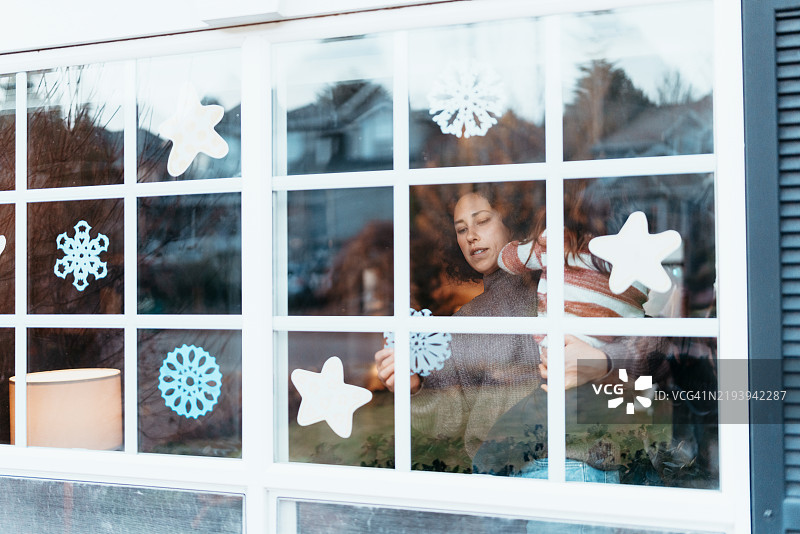 欧亚女性在家中窗户上挂雪花装饰图片素材