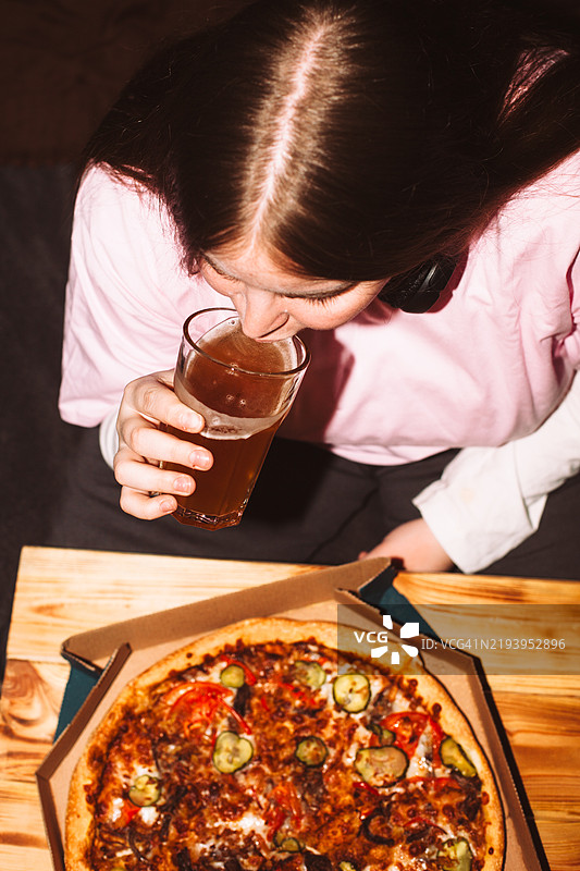 年轻女性坐在桌旁喝啤酒，旁边有比萨饼图片素材