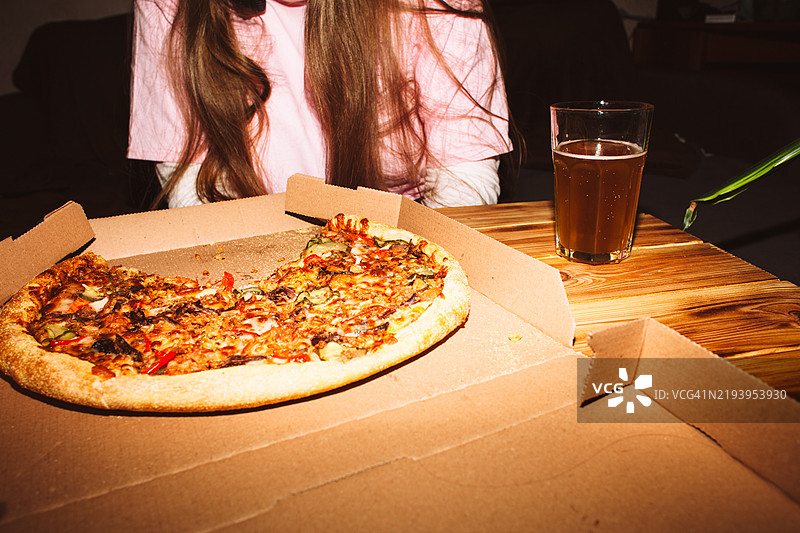 年轻女性在家派对上坐在桌子旁，享用比萨和啤酒图片素材