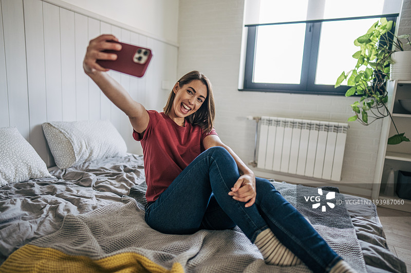一位短发且有酒窝的女性在舒适的床上微笑着拍摄俏皮的自拍照图片素材