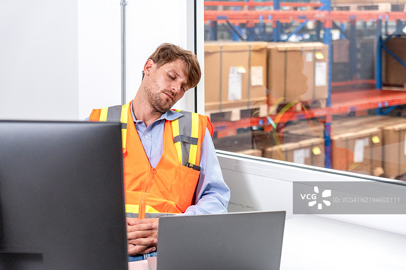 年轻疲惫的仓库工人在工作场所睡觉，因加班而感到精疲力竭。留白空间。图片素材