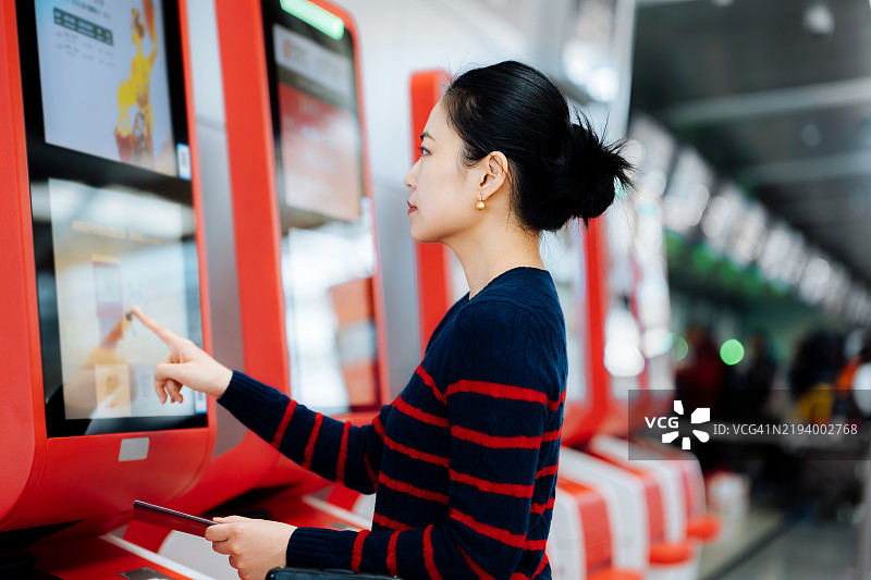 亚洲女商人在机场航站楼使用自助值机机获取登机牌，机场科技。乘客在机场用智能手机扫描票据。图片素材