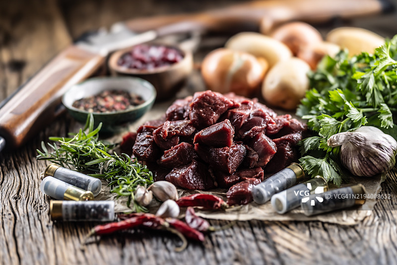 切片的新鲜野猪肉，配以迷迭香香料和蔓越莓酱。装饰有一把带子弹的猎枪。图片素材