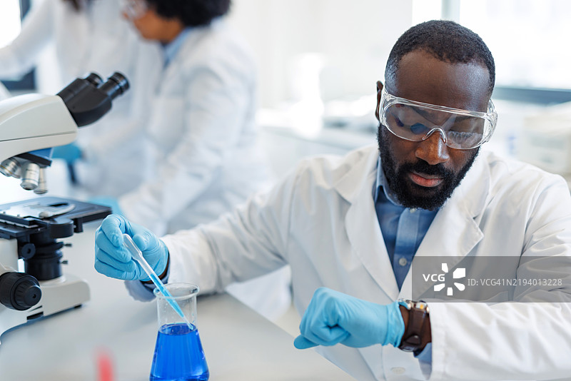 科学家在实验室中查看时间，同时滴加蓝色液体图片素材