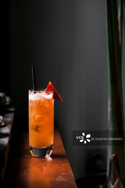 优雅的百香果鸡尾酒，配有朗姆酒、酸甜混合饮料和辣椒装饰，盛在高脚杯中，背景昏暗而富有情调，现代调酒和奢华酒吧概念图片素材