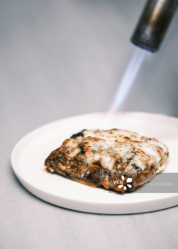 烤制至金黄色外壳的茄子帕尔马干酪，传统意大利菜，层层叠叠的茄子、番茄酱和马苏里拉奶酪，餐厅环境中的精致餐饮呈现。图片素材