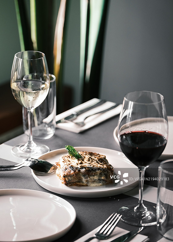 意大利餐厅中供应的茄子帕尔马干酪，搭配红酒和白酒，经典的分层菜肴，配有马苏里拉奶酪、番茄酱和帕尔马干酪，精致的餐桌布置图片素材