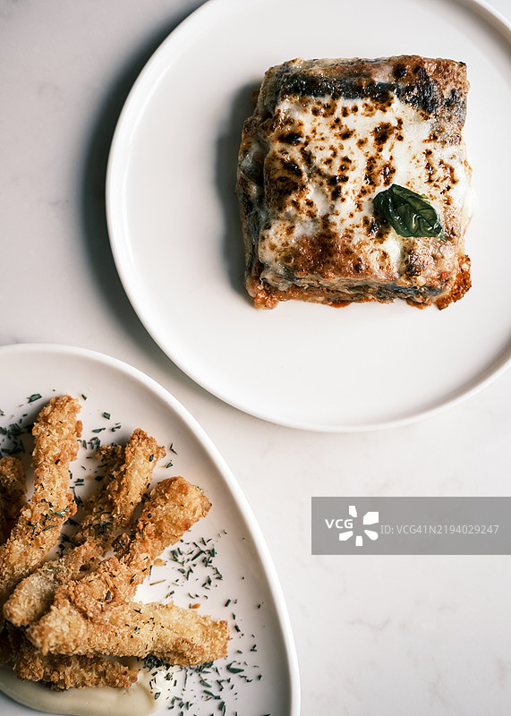 正宗意大利菜肴：茄子帕尔马干酪和炸牛肚，盛放在优雅的白色盘子上，精致的美食呈现，丰富的质感和地中海风味。图片素材