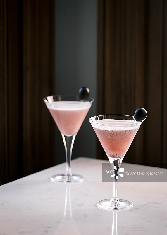 两杯粉色鸡尾酒盛在优雅的马提尼酒杯中，搭配樱桃装饰，放在大理石桌上，时尚的酒吧氛围，精致的调酒艺术，优雅的晚间饮品，意大利餐厅的美学图片素材