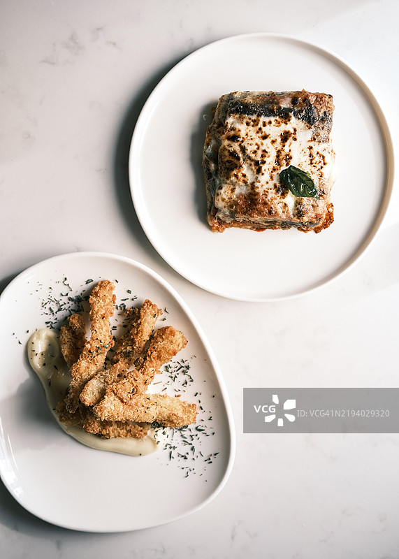 正宗意大利菜肴：茄子帕尔马干酪和炸牛肚，盛放在优雅的白色盘子上，精致的美食呈现，丰富的质感和地中海风味。图片素材