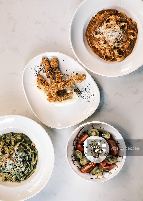经典意大利菜肴的平铺展示，包含肉酱宽面条、香蒜宽面条、布拉塔沙拉和脆皮炸肚，正宗地中海美食与精致的摆盘。图片素材