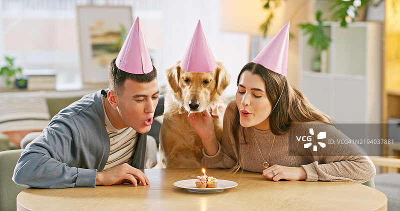 情侣在公寓里庆祝生日，吹灭蛋糕上的蜡烛，身边有他们的狗。家中有动物和人们，庆祝收养纪念日，享用零食，陪伴着金毛猎犬。图片素材