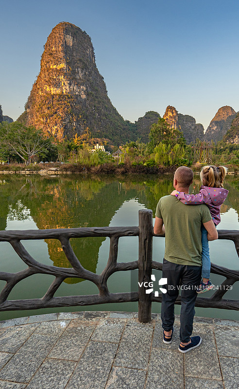 父亲和女儿在桂林阳朔县的遇龙河风景区欣赏令人叹为观止的美景和戏剧性的石灰岩地貌的倒影图片素材