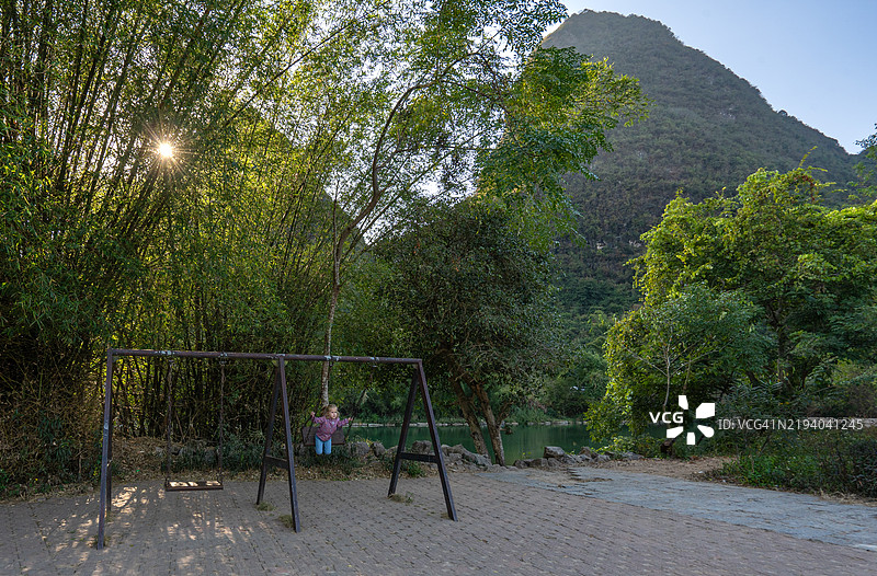 在广西桂林阳朔县的遇龙河风景区，年轻女孩在秋千上，背景是令人叹为观止的美丽风景和戏剧性的石灰岩地貌。图片素材