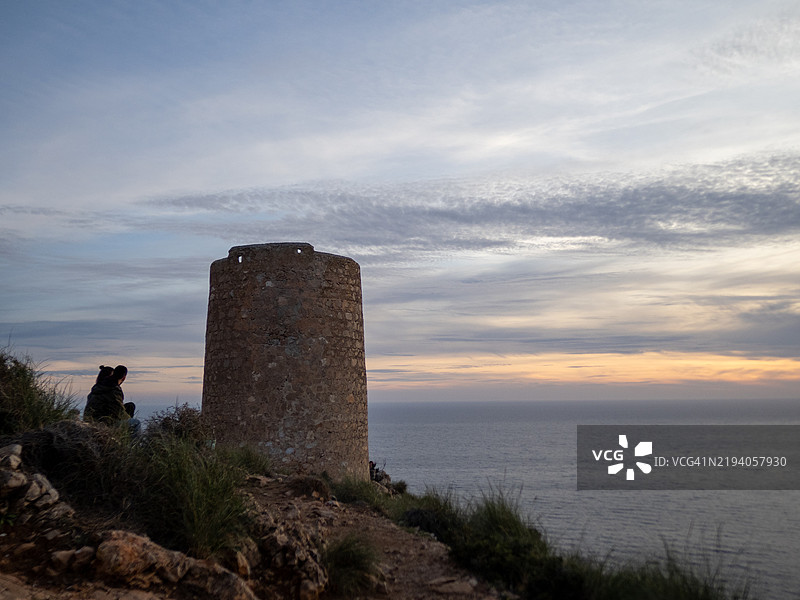 游客在悬崖上的古塔旁观看海上的日落图片素材