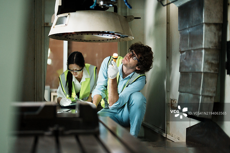 两名工厂技术人员在现代工业环境中使用工具和手电筒检查机器设备图片素材