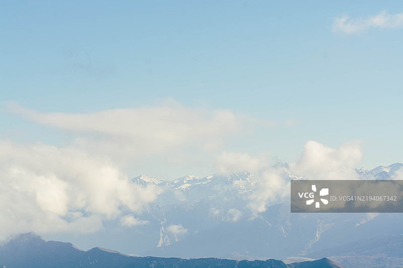 明亮蓝天中，低云掩映着雪山峰。图片素材