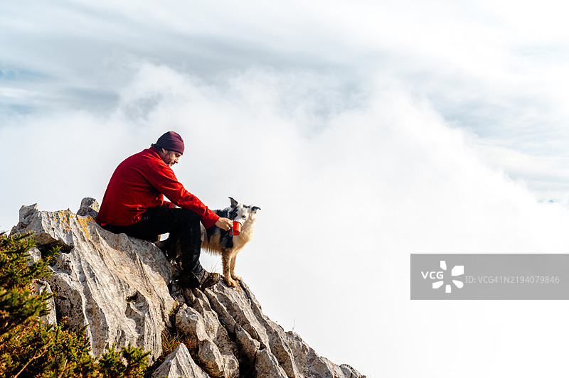 登山者在云层之上的山顶与他的狗分享饮料图片素材