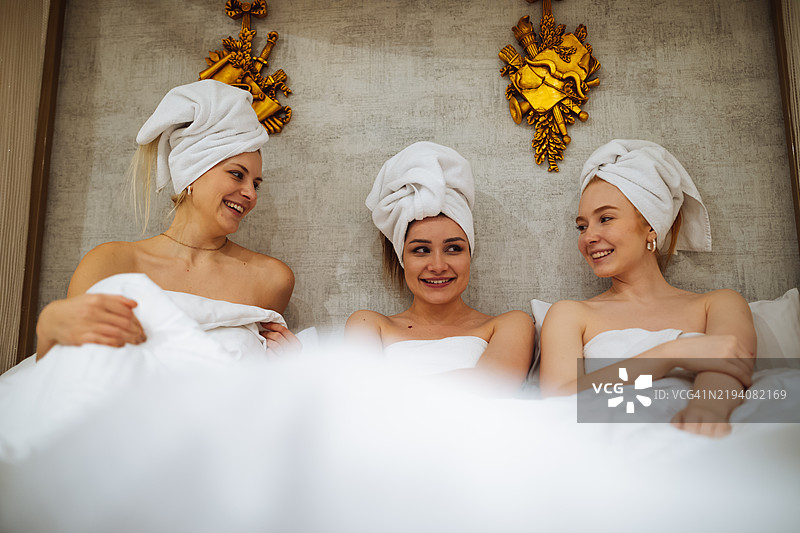 三位头上裹着毛巾、身穿白色浴袍的女性。适合用于水疗、美容和友谊主题的图片。图片素材