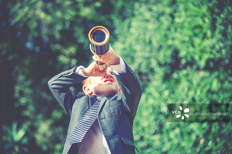 一个穿着西装的孩子在用望远镜观察图片素材