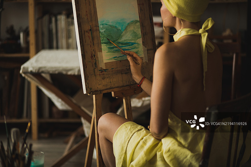 身穿黄色的艺术家在阳光明媚的工作室环境中创作画作图片素材