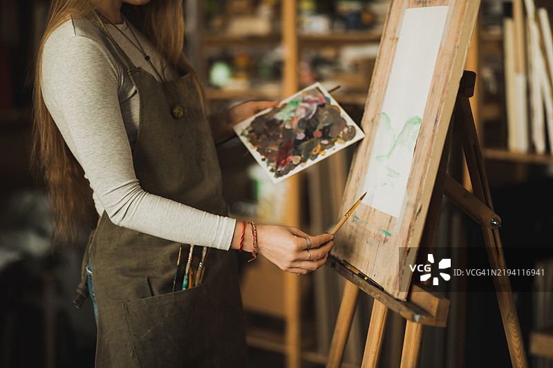 女性艺术家的手在画布上作画，手持调色板，身处创意工作室图片素材