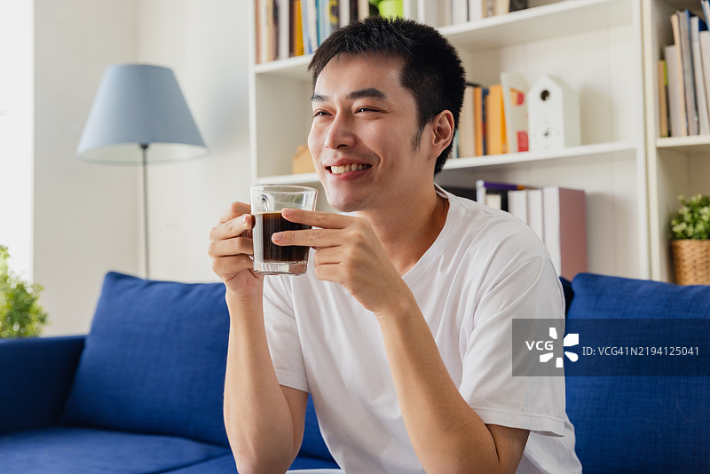 男人在舒适的客厅里享受一杯咖啡，四周摆满了书架。图片素材