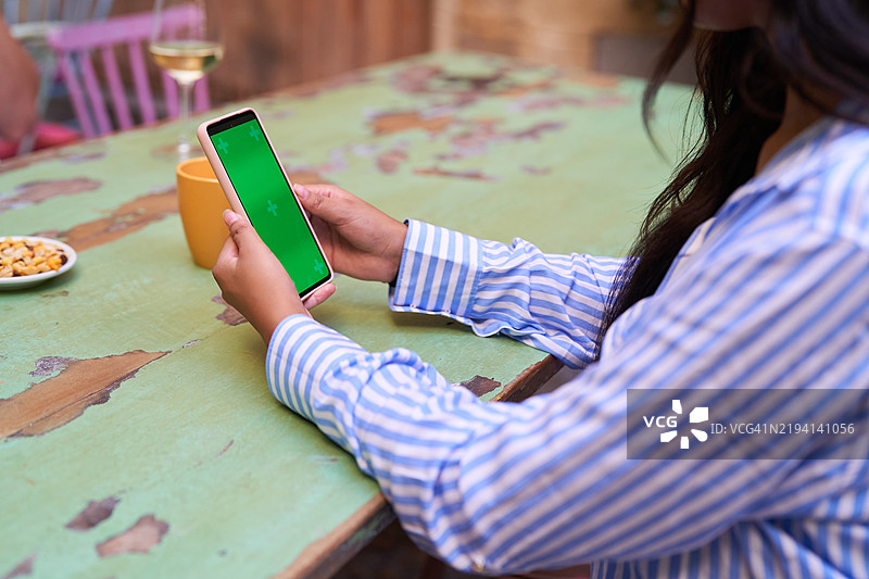 在餐厅里使用带有绿色屏幕的智能手机的女性图片素材