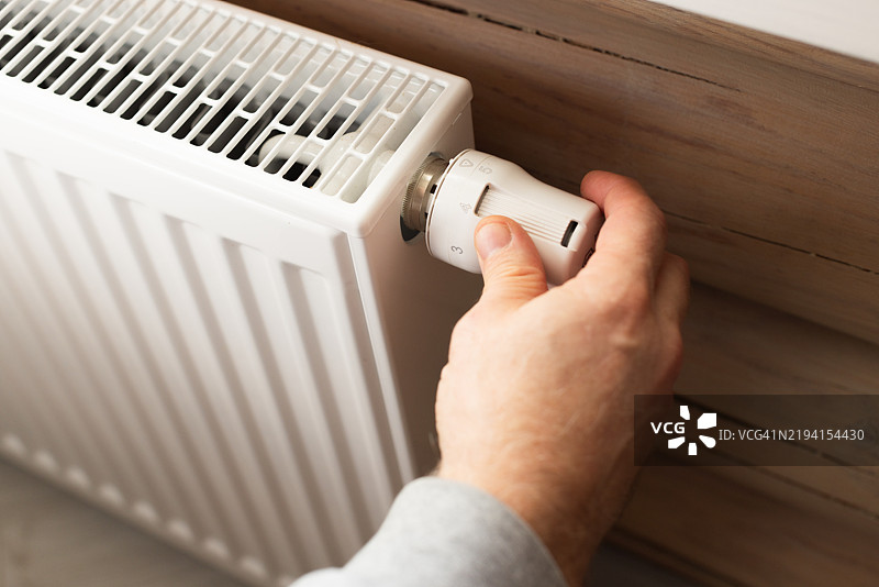 一名男子在寒冷天气来临时调高暖气散热器的温度图片素材
