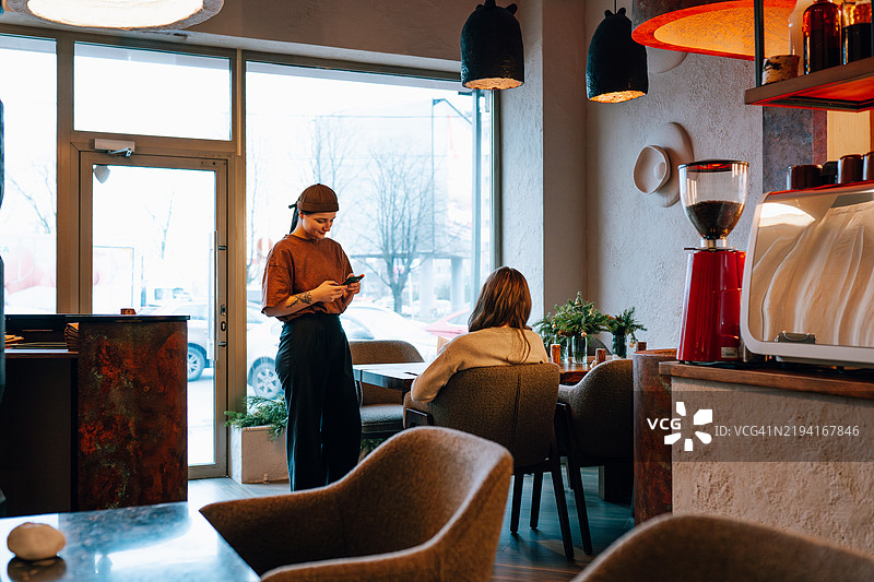 现代咖啡店的女服务员使用智能手机等待顾客图片素材