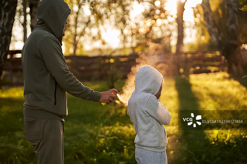 一名男子在森林里给一个孩子喷洒驱虫剂。图片素材
