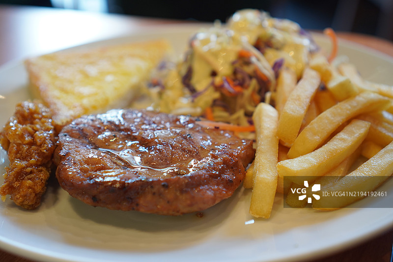 白盘上的牛排、猪肉、蔬菜沙拉、吐司和薯条，准备好享用的美食图片素材