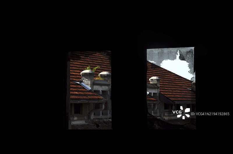 黑暗房间窗外的红色屋顶和烟囱景象。图片素材