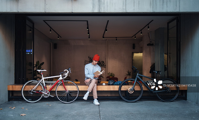 在户外咖啡馆阅读书籍的男子，旁边停放着自行车图片素材
